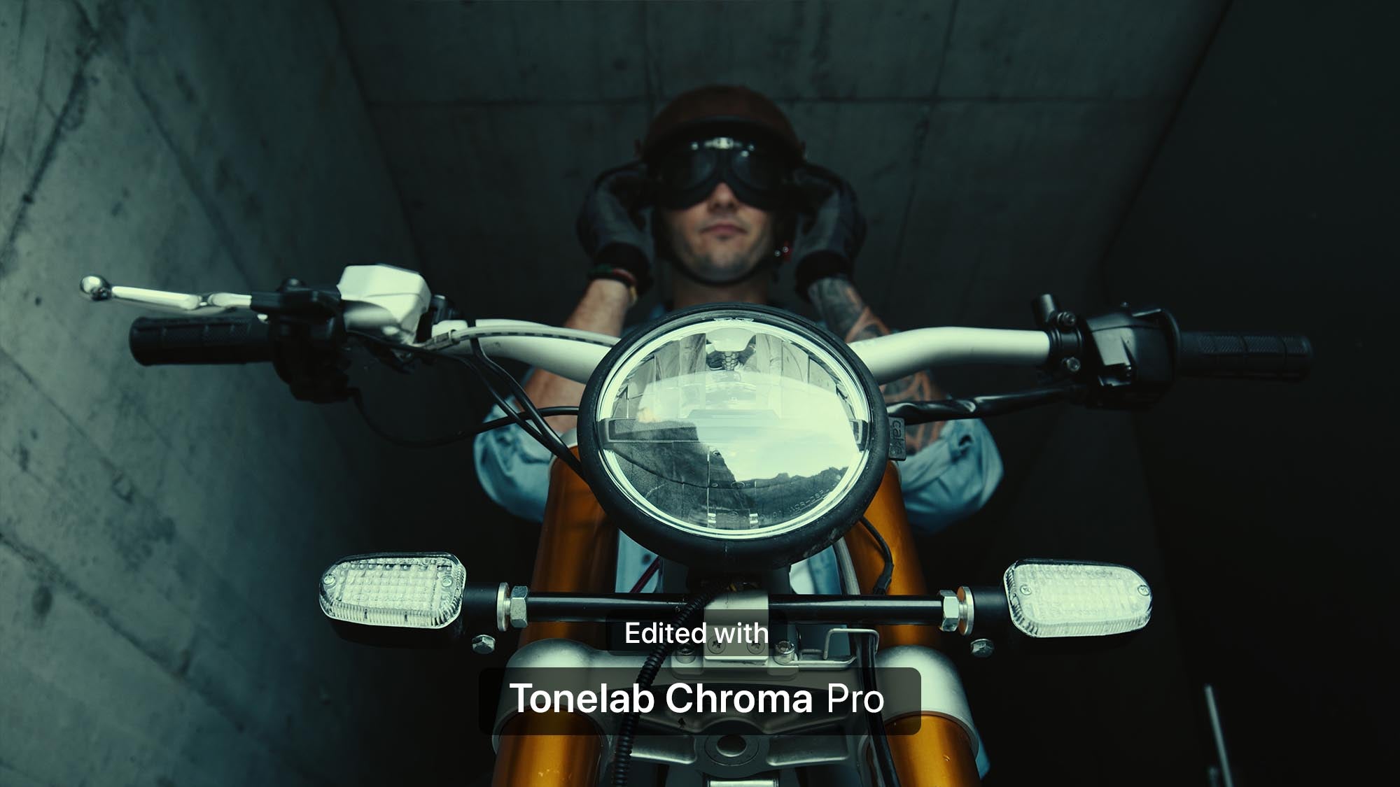 A low-angle shot of a person wearing a brown beanie, black sunglasses, and a light blue denim jacket, sitting behind the handlebars of an orange motorcycle inside a dark concrete tunnel. Text overlay at the bottom reads 'Edited with Tonelab Chroma Pro'.
